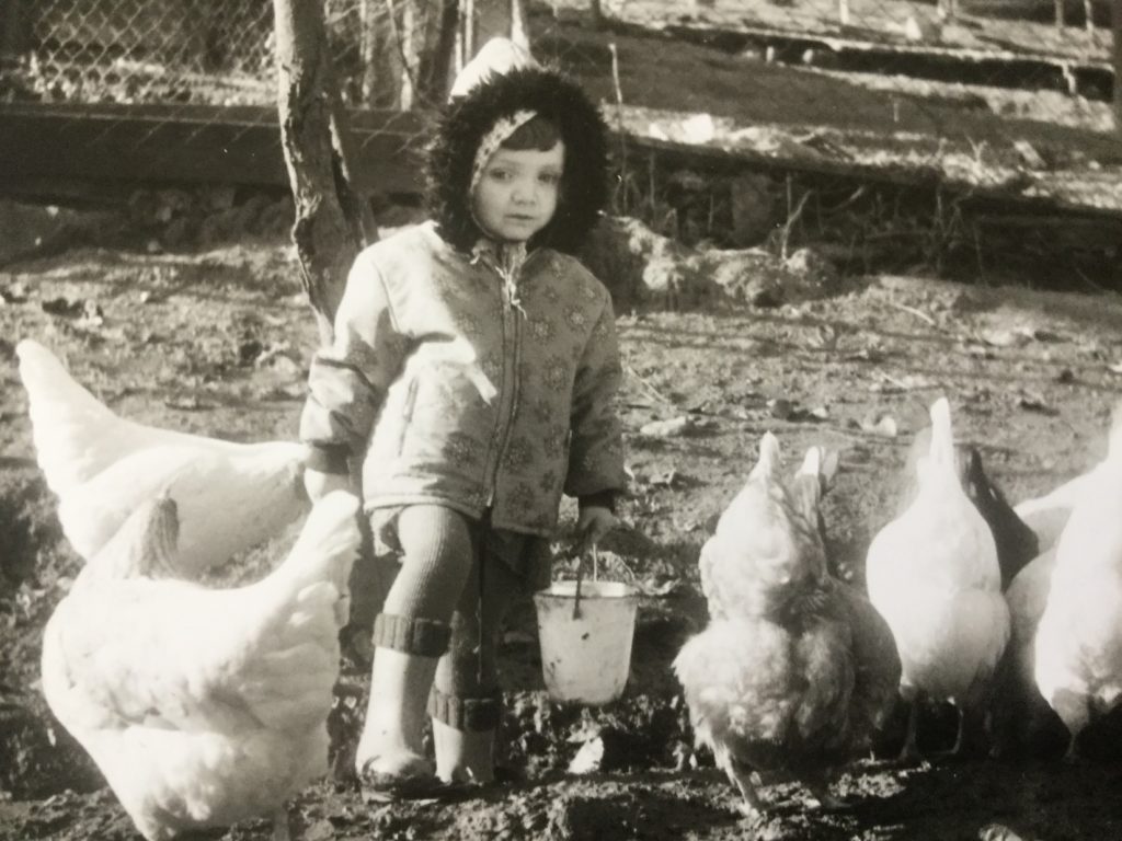 Sonja Eisenbeiß als Kind mit Hühnern und einem Futtereimer vor einem Baum im Gehege